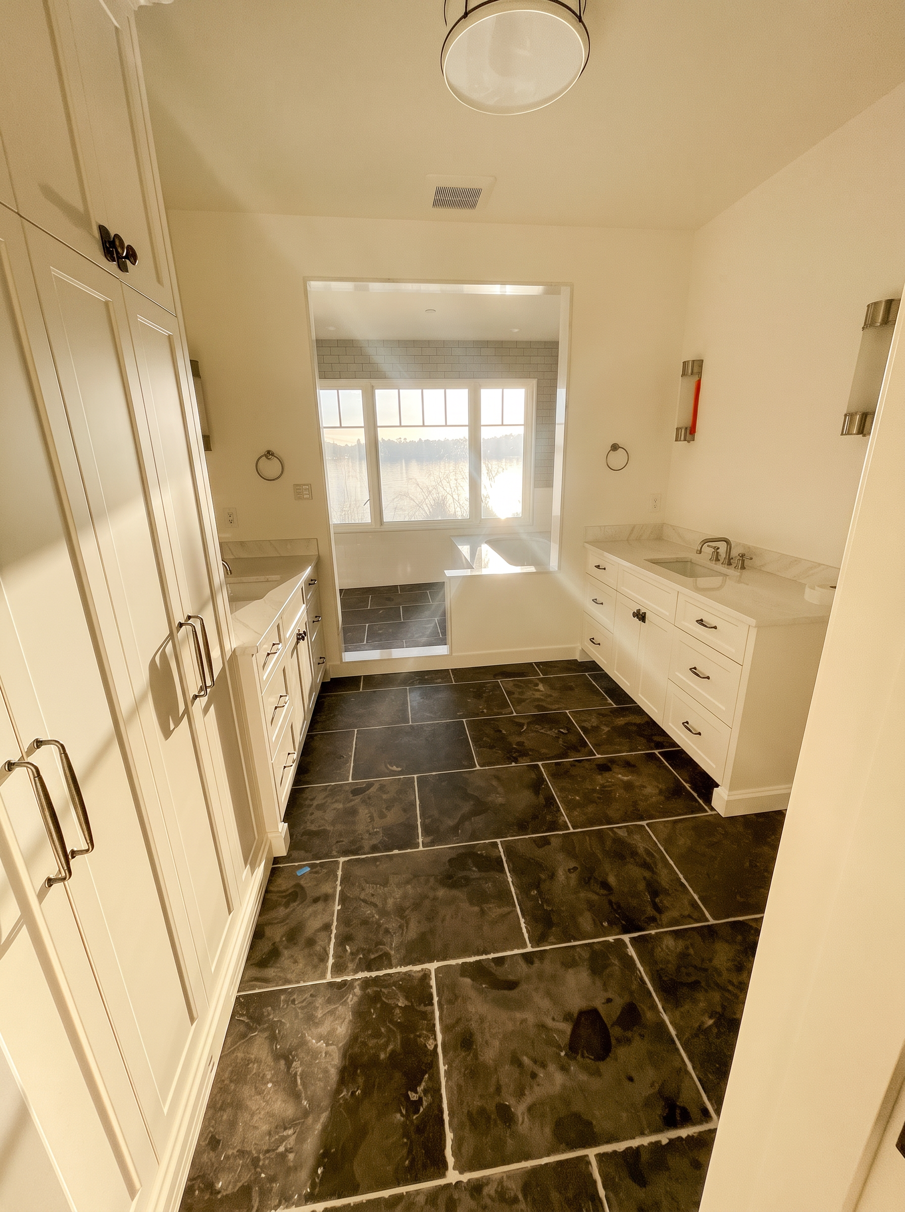 Bright bathroom with white shaker cabinetry, marble countertops, and a coastal view